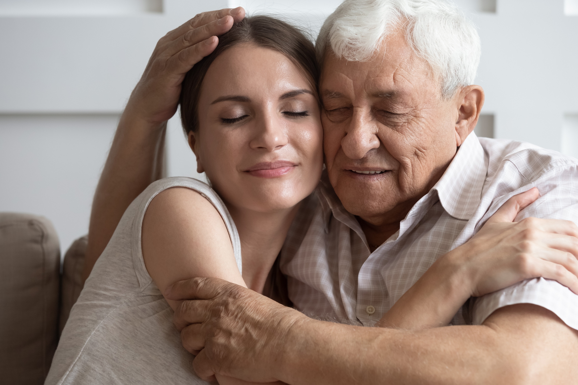 A woman hugs her elderly father, diagnosed with dementia, both with eyes closed, showing care and affection