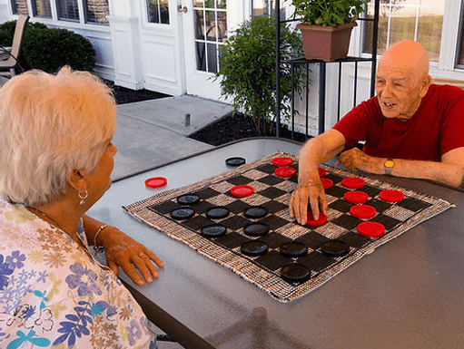 Home 5 Two senior residents enjoy a friendly game of checkers outdoors at Abbey Manor, a vibrant senior care community