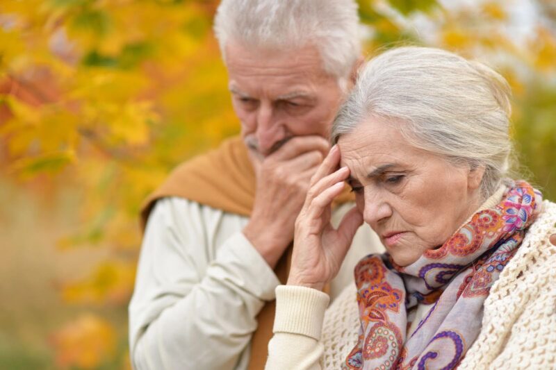 An elderly couple showing concern, the woman holds her head with worry, symbolizing the emotional impact of a dementia diagnosis