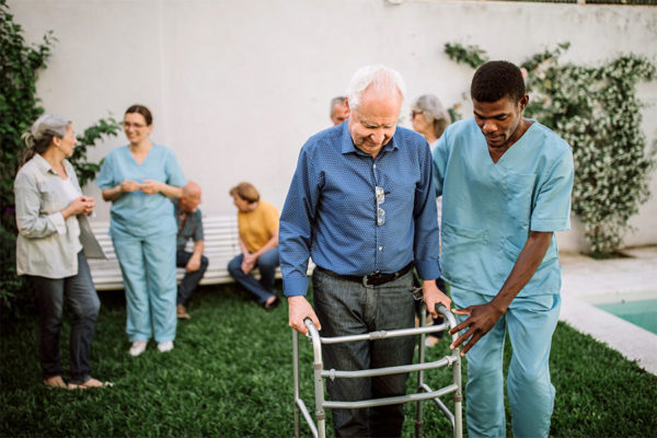Caregiver assisting senior man in walking.