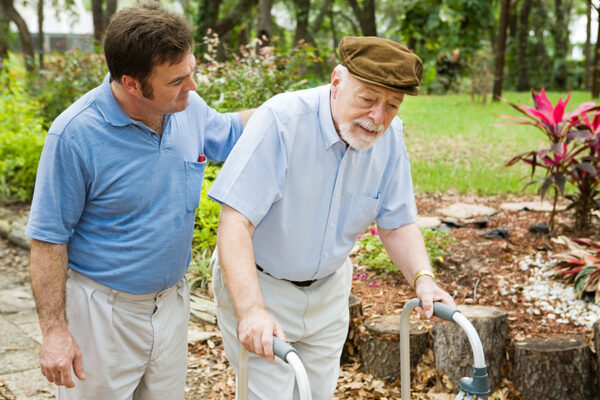 Caregiver encouraging senior man to walk; promoting independent living