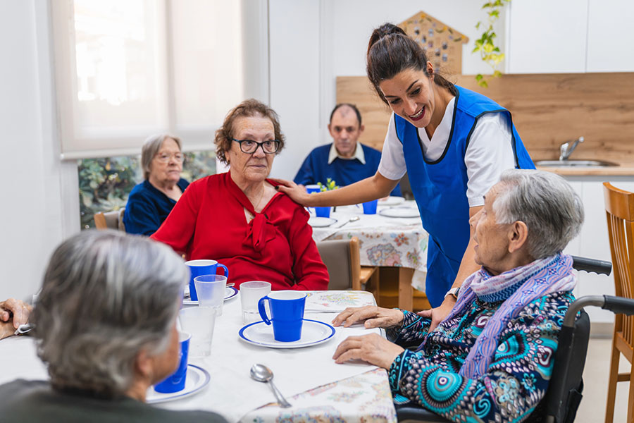 Friendly caregiver supporting senior residents in a bright dining room, showcasing supportive care options like assisted living after hospital discharge at Abbey Manor.