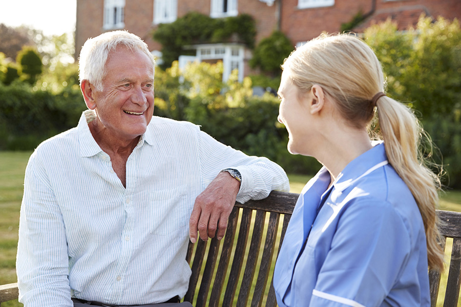 Senior resident talking with caregiver outdoors at senior living facility community garden.