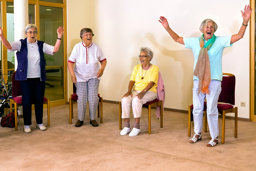 Seniors participating in group chair exercises inside Assisted living facilities community room.