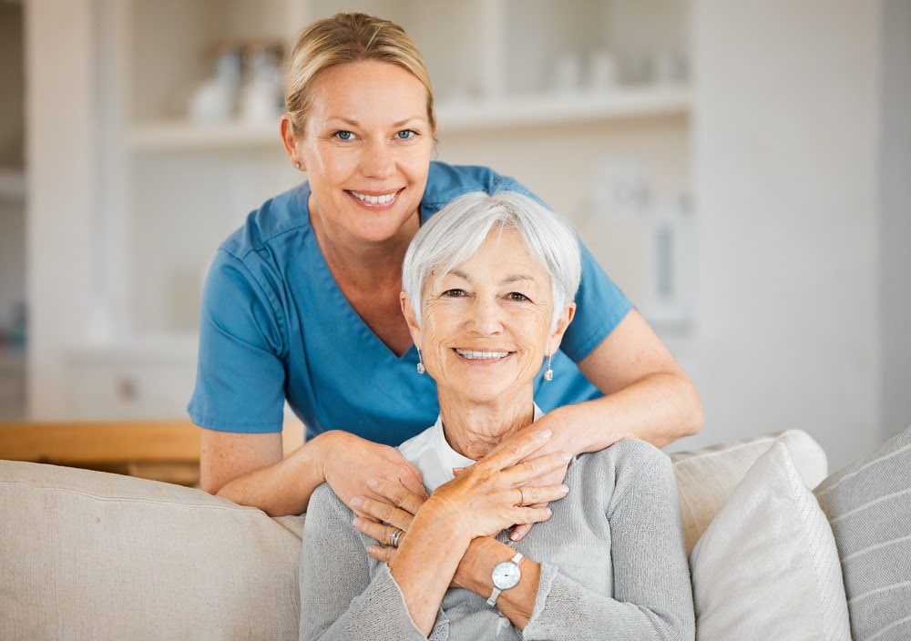 Nurse embracing senior woman in a cozy residential assisted living setting, both smiling warmly