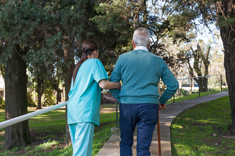A caregiver assists a senior man walking outdoors, representing professional respite care services.