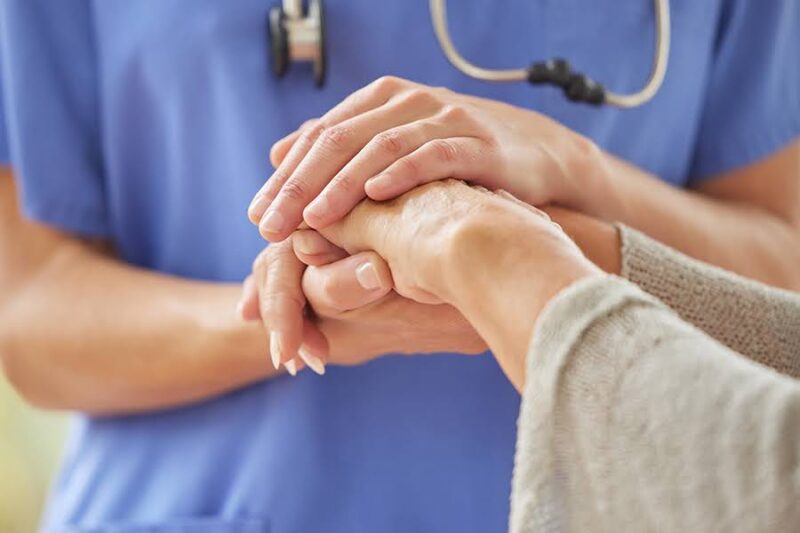 A caregiver holding an elderly person's hand, providing support, illustrating what are the signs of early dementia in a family