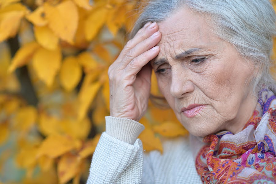 An elderly woman with a hand on her forehead, appearing concerned, illustrating what are the earliest signs of dementia