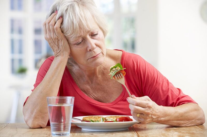 An elderly woman with a sad expression, staring at food, illustrating what is the early stage of dementia
