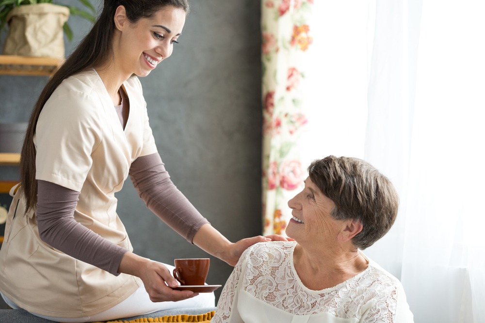 Friendly caregiver giving tea to senior lady.