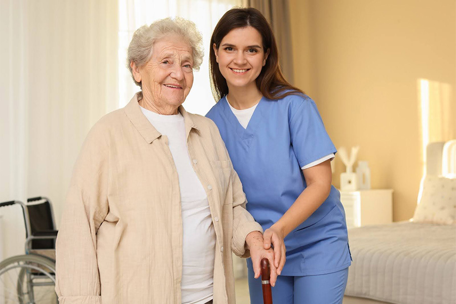 Caregiver assisting an elderly woman with a cane in a bright room, representing compassionate dementia care near White Plains, Wicomico County, MD Caregiver assisting an elderly woman with a cane in a bright room, representing compassionate dementia care near White Plains, Wicomico County, MD