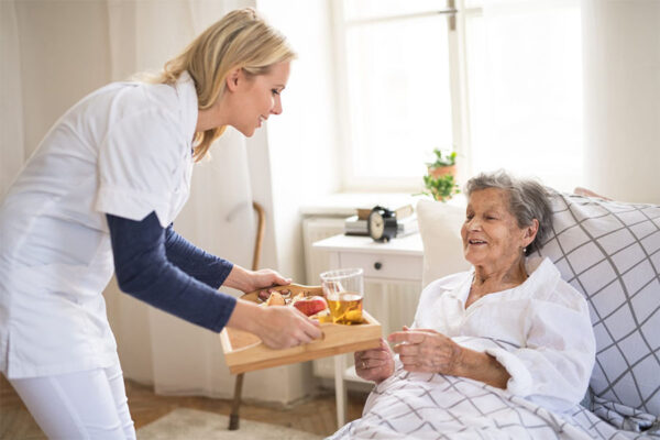 Caregiver providing nourishment to senior woman in her bed concept image for what is respite care for seniors