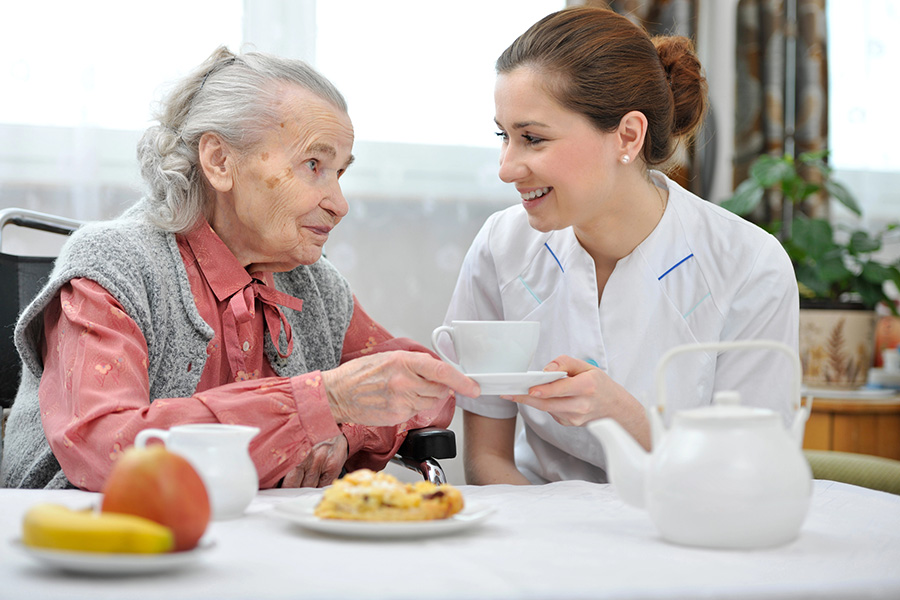 Caregiver serving tea to an elderly woman to support nutrition and address lack of appetite in elderly