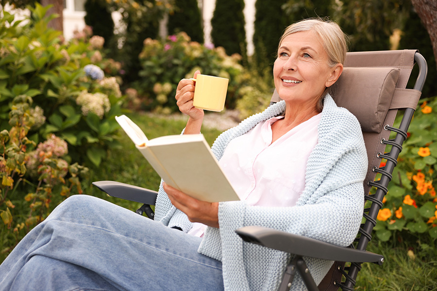 Caregiver taking a quiet moment to rest while reading a book and holding a mug in a peaceful garden setting
