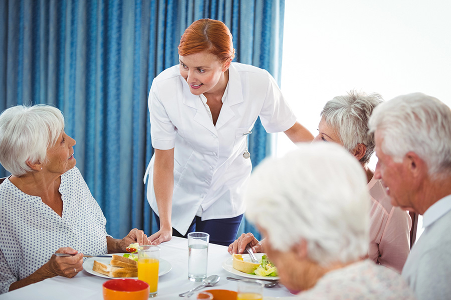Caregiver talking with seniors at lunch, supporting nutrition to address loss of appetite in older adults