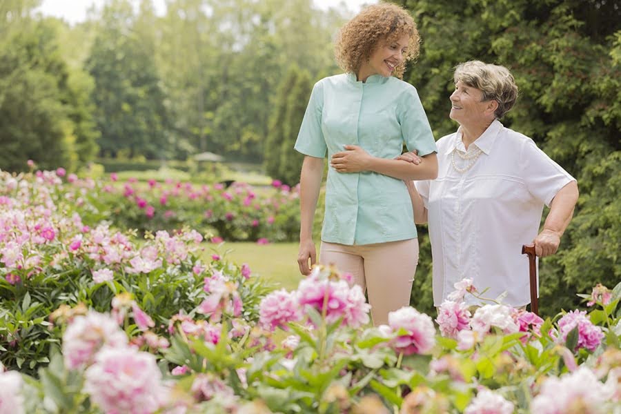 Caregiver walking with elderly woman in a garden, offering support and companionship for vascular cognitive impairment (VCI)