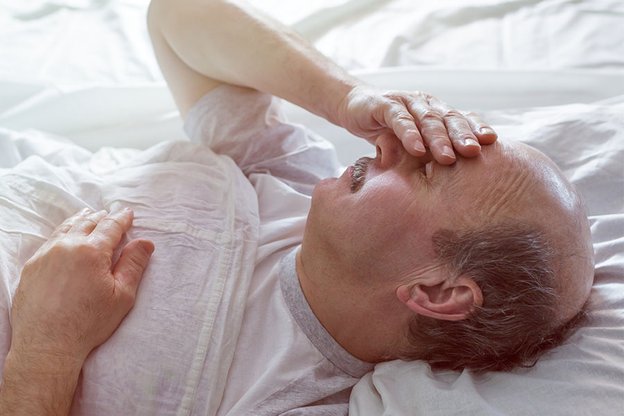 Older man lying in bed holding his forehead in confusion, showing signs of sudden delirium in seniors. Older man lying in bed holding his forehead in confusion, showing signs of sudden delirium in seniors.
