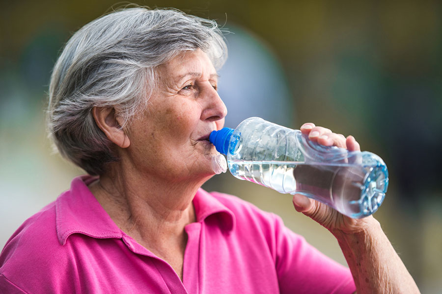 Senior woman drinking water from a bottle to stay hydrated during recovery from illness. Senior woman drinking water from a bottle to stay hydrated during recovery from illness.