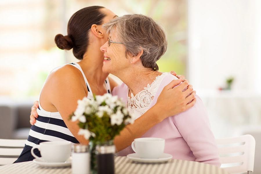 Older woman hugging her daughter at a café table, showing care and support during stages of vascular dementia