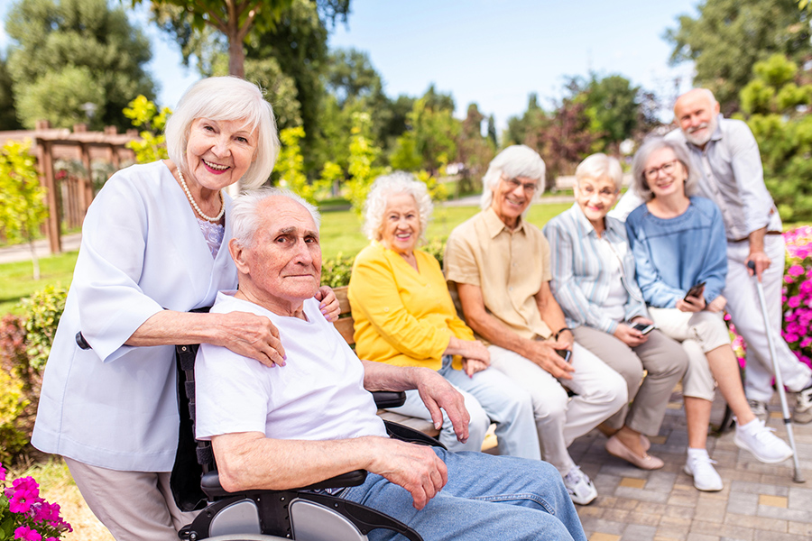 Seniors smiling together in a sunny outdoor garden park, highlighting community and social engagement in senior living.