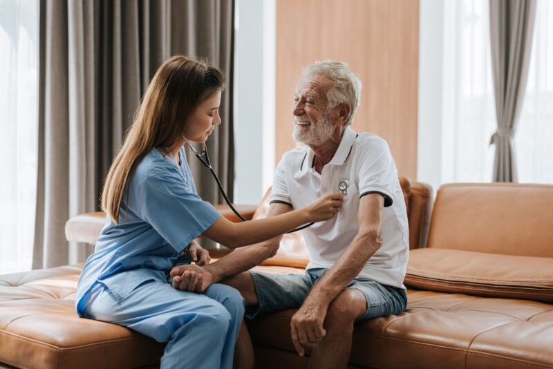 A caregiver checking an elderly man's heart with a stethoscope, illustrating personalized senior care planning for health monitoring