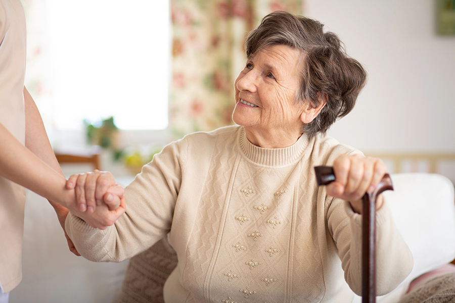 Caregiver helping a senior resident stand with a cane at a community offering assisted living near Bethany Beach, DE.