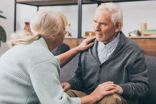Confused elderly man suffering from dementia is being helped by his wife.