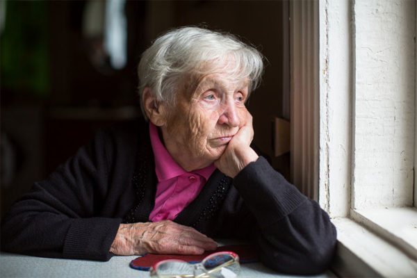 Elderly woman looking out the window concept image for depression in seniors.