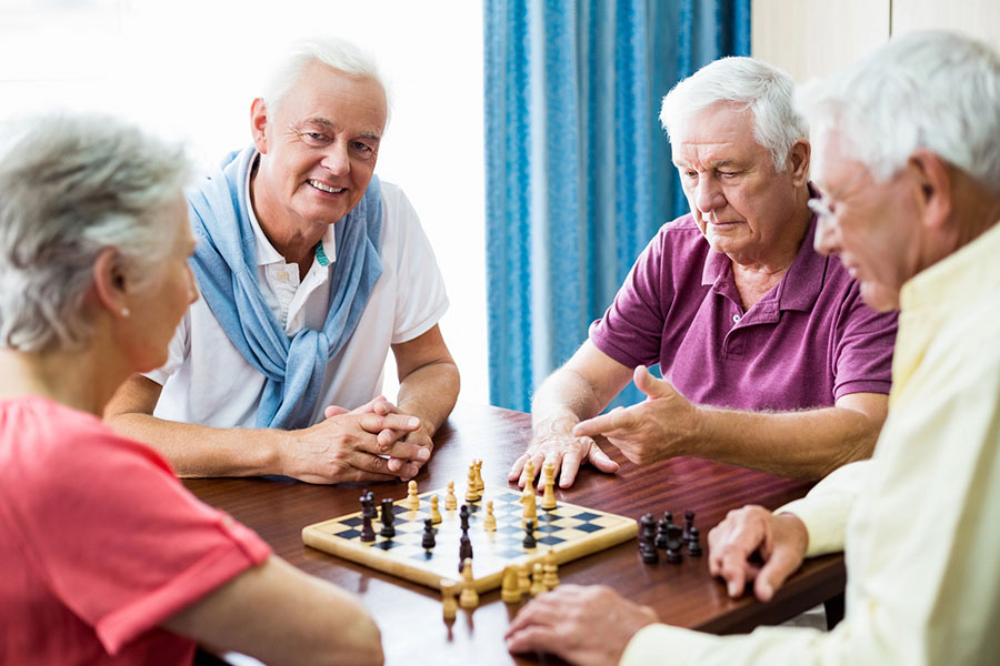 Four elderly residents gathered around a chessboard enjoying friendly competition and daily assisted living activities near Selbyville.