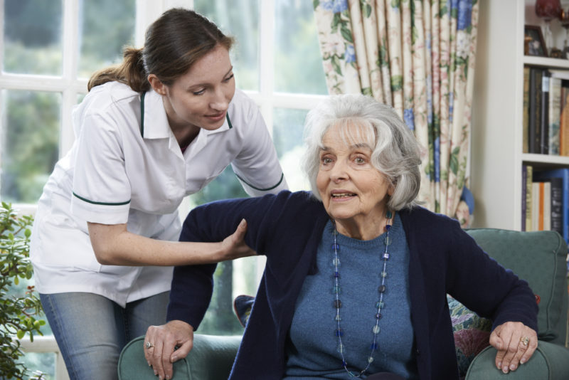 Care Worker Helping Senior Woman To Get Up Out Of Chair Respite care services